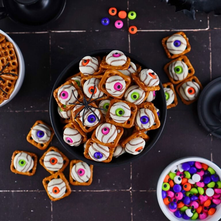 Bowl of pretzel treats decorated like colorful monster eyes on a dark table.