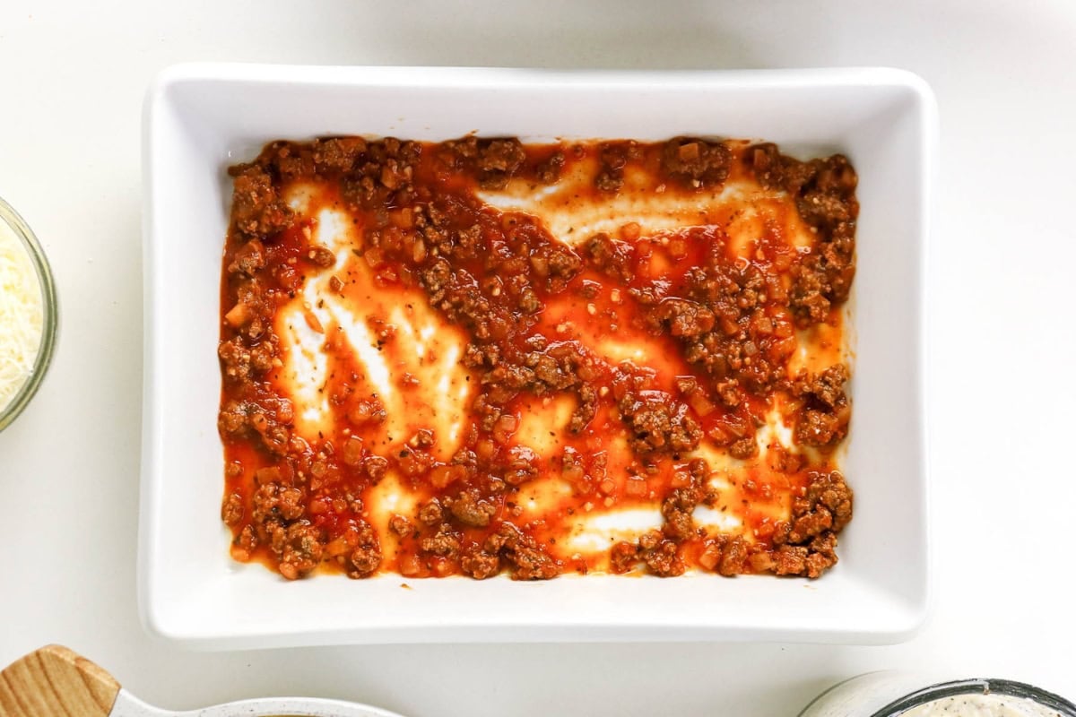 Ground meat and tomato sauce spread in a white rectangular baking dish.