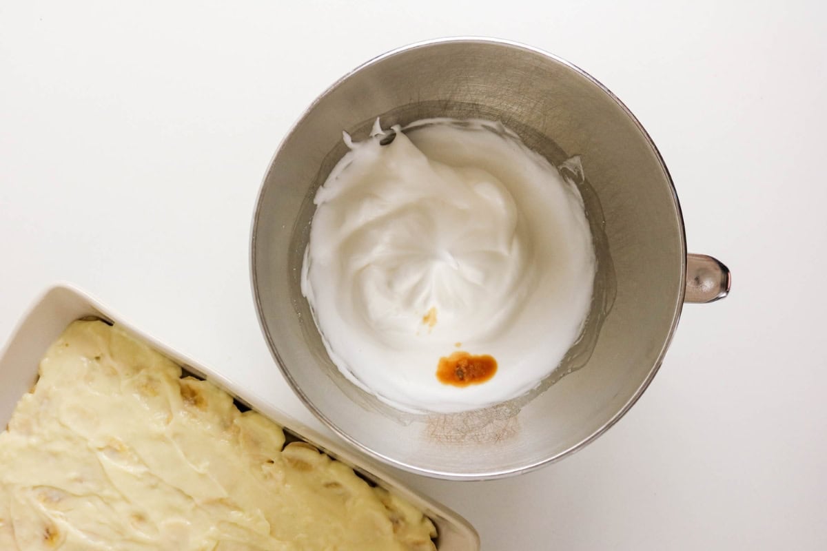Metal bowl with whipped egg whites and vanilla next to a dish with batter.