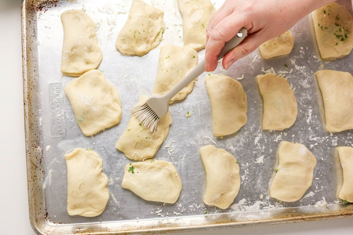 Hand brushing dumplings with egg wash on a baking sheet before baking.