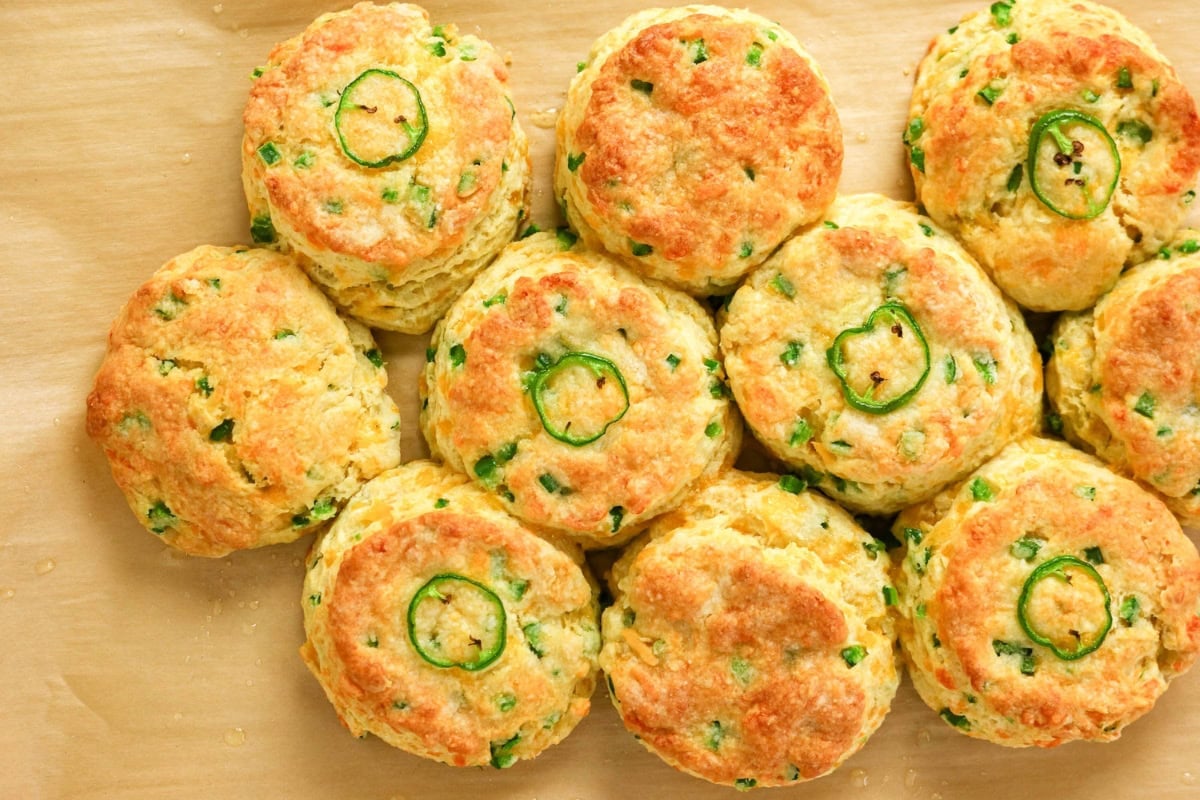 Golden biscuits with green jalapeño slices and herbs on top, arranged closely.