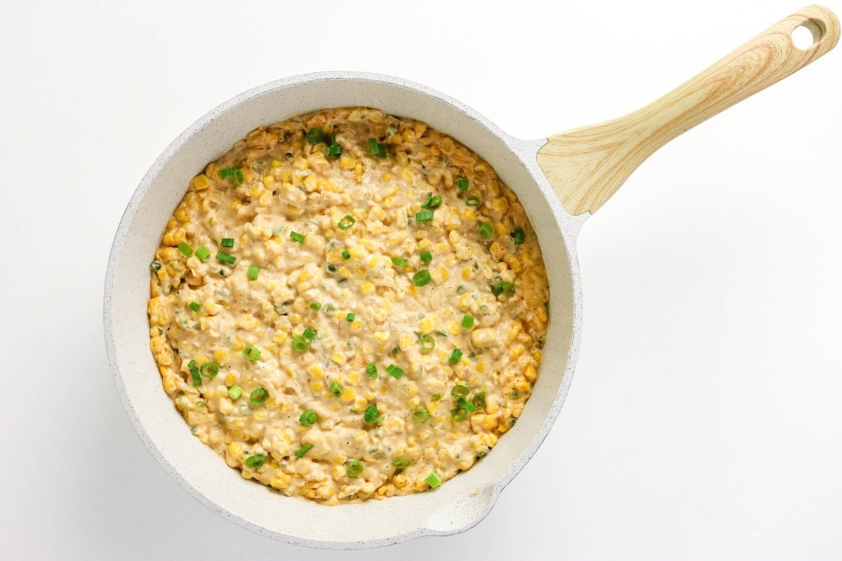Creamy corn dip topped with chopped green onions in a white skillet.