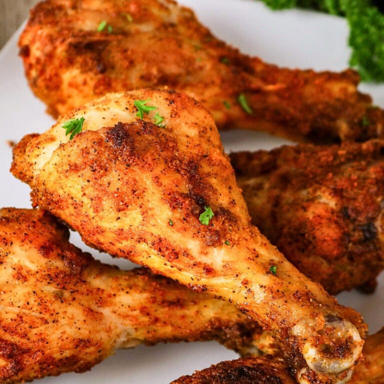 Close-up of seasoned baked chicken drumsticks garnished with fresh herbs.