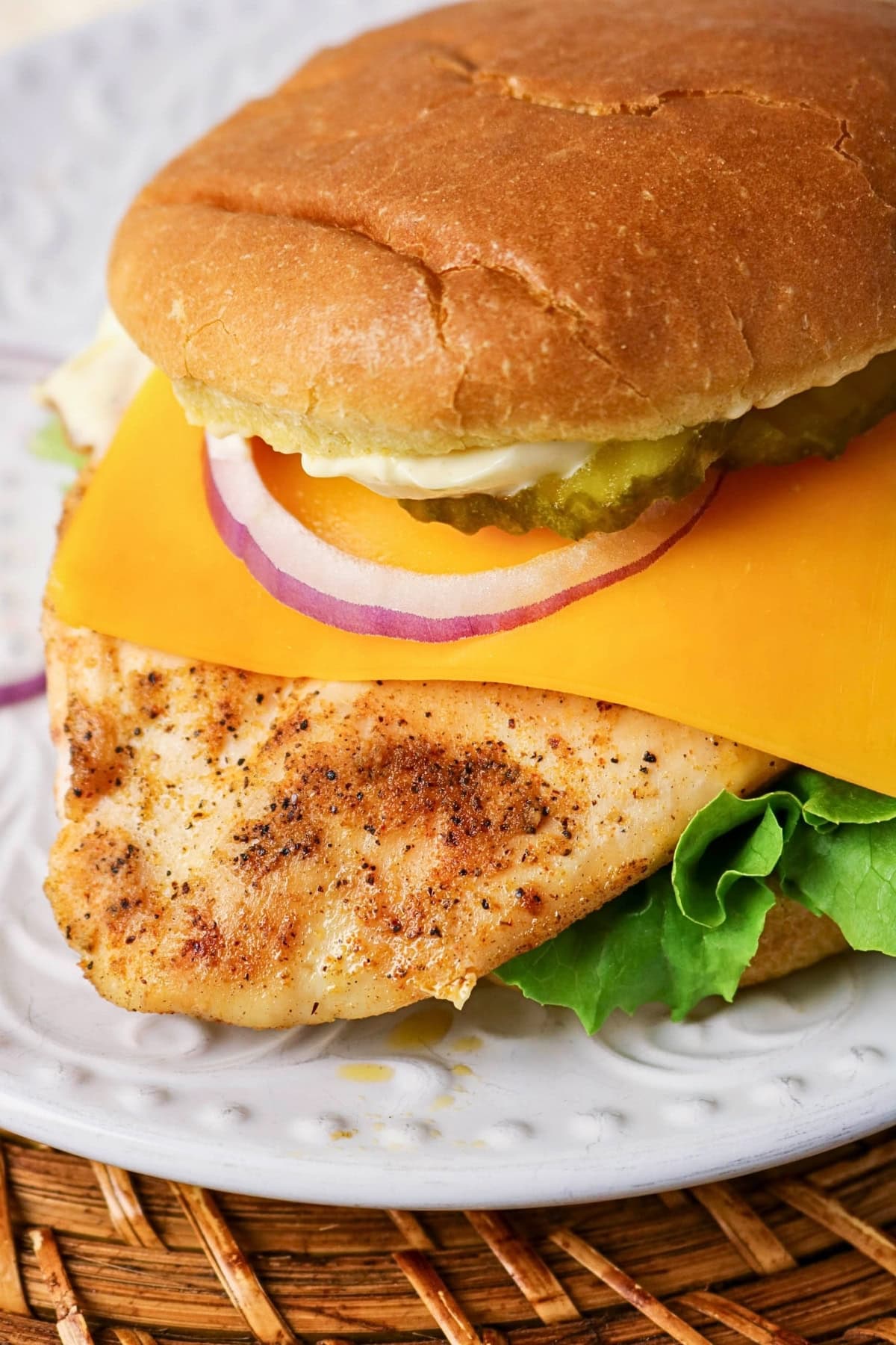 Grilled chicken sandwich with cheese, pickles, lettuce, and onion on a bun.
