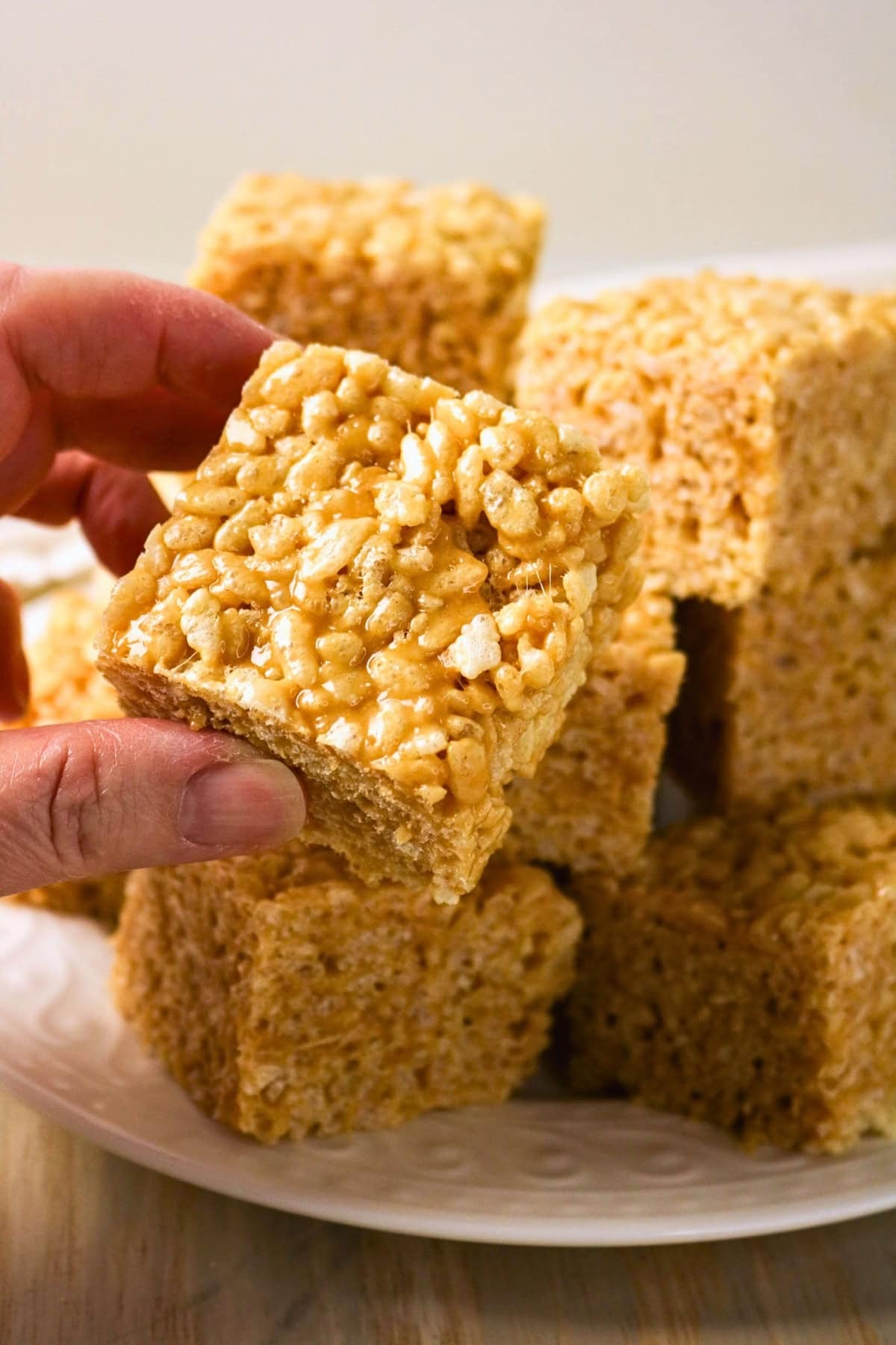 A hand holding a square rice crispy treat above a plate of more treats.