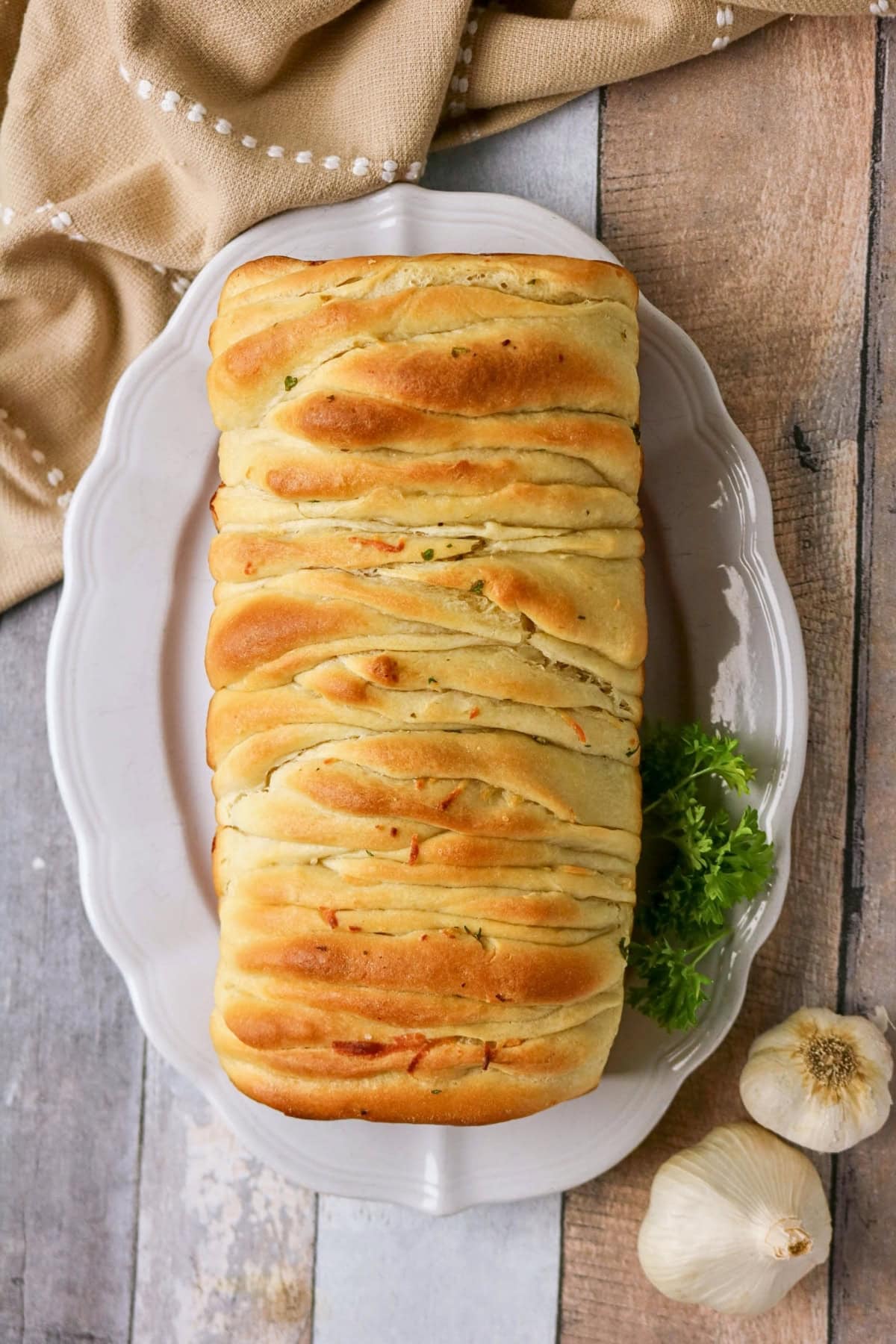 Golden pull-apart bread loaf on a white platter with parsley and garlic.