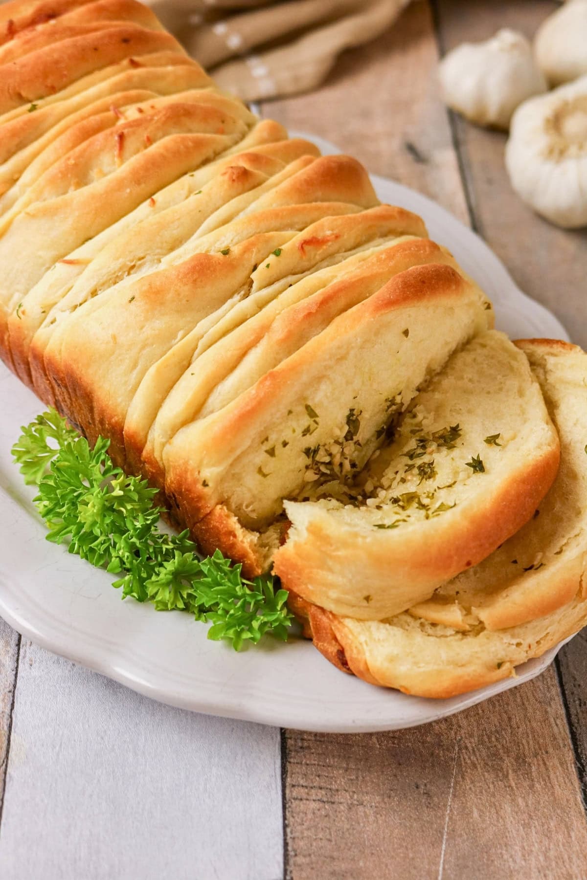 Sliced garlic pull-apart bread on a white plate with parsley garnish.