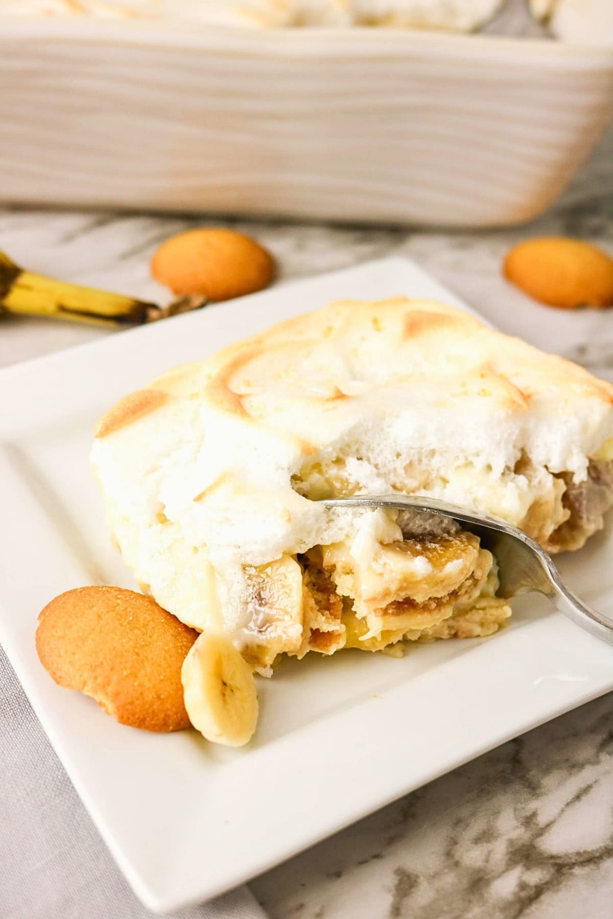 A serving of banana pudding with vanilla wafers on a white plate, with a fork.