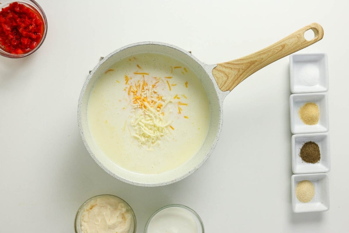 White sauce with shredded cheese in a pan, surrounded by spices and toppings.