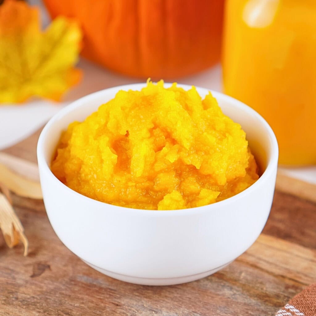 Bright orange pumpkin puree in a white bowl on a wooden surface.