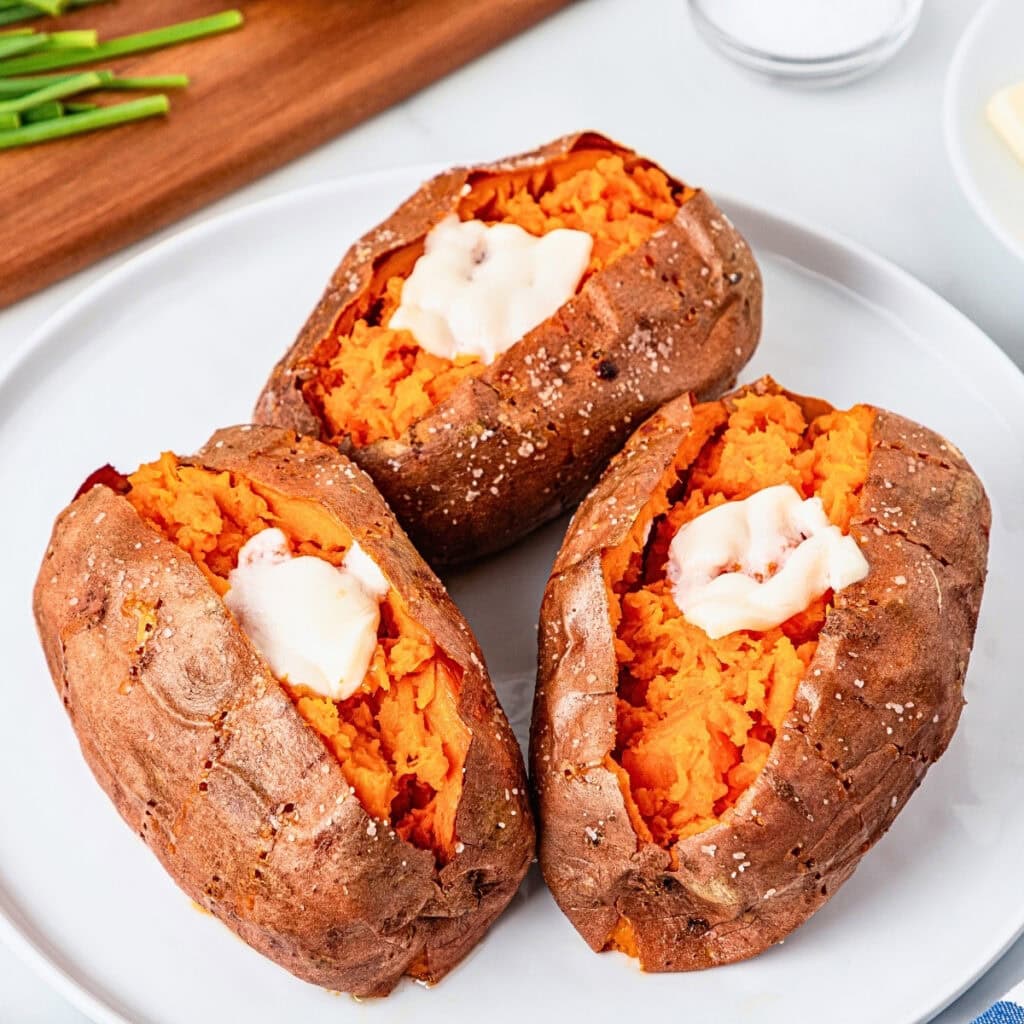 Three baked sweet potatoes with melted butter on a white plate.