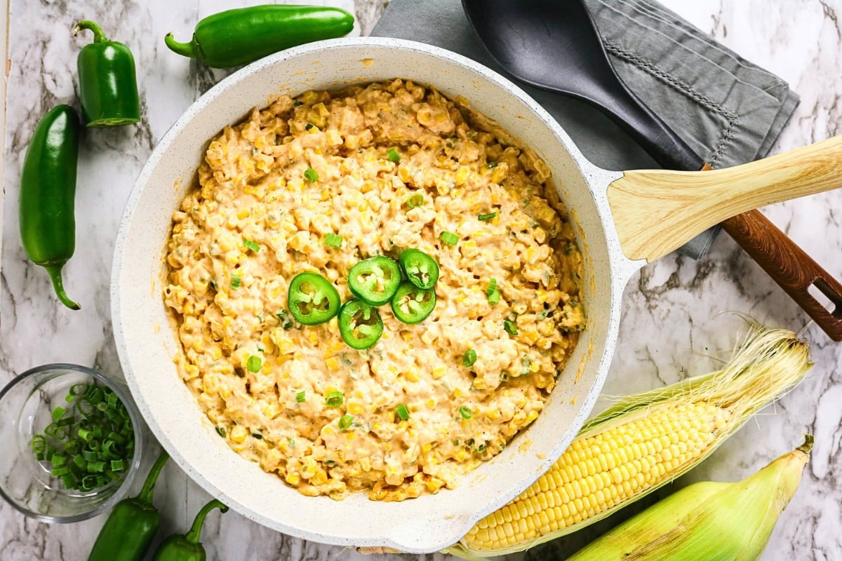 Creamy corn dip topped with jalapeno slices in a skillet, with corn and peppers.
