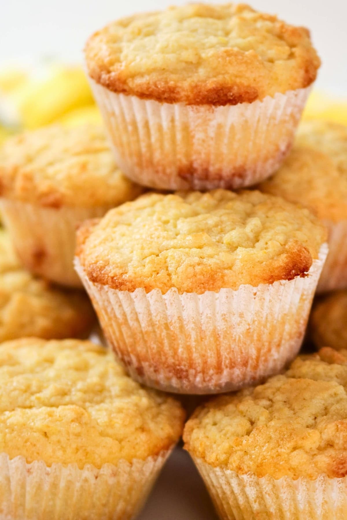 A stack of golden, freshly baked muffins in white paper liners.