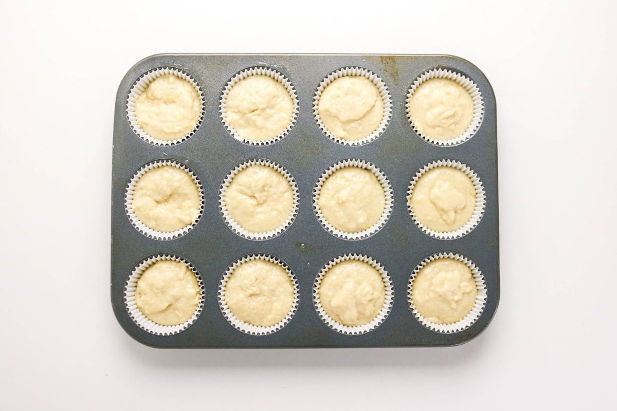 A muffin tin with 12 unbaked cupcakes in white paper liners.