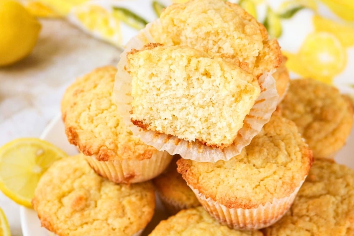 Lemon muffins, one cut in half, stacked on a plate with lemon background.