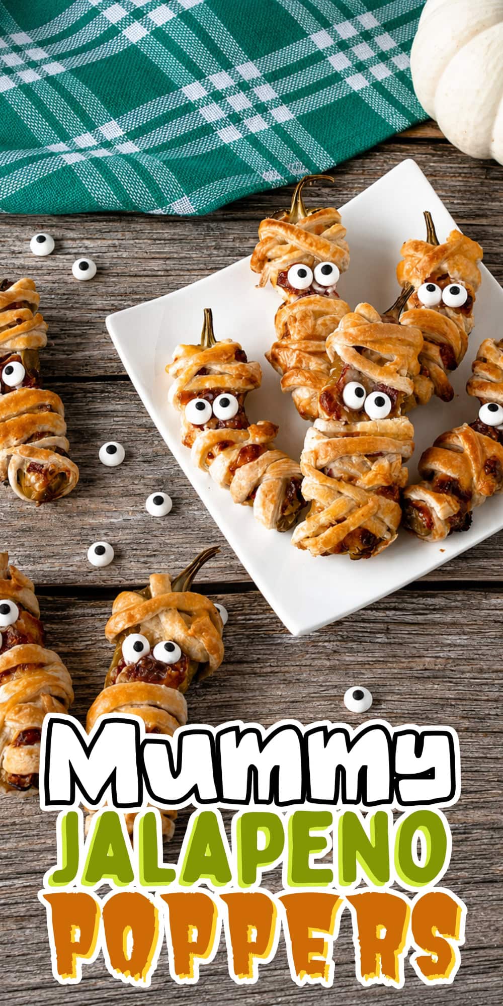 Jalapeno poppers wrapped like mummies with candy eyes on a wooden table.
