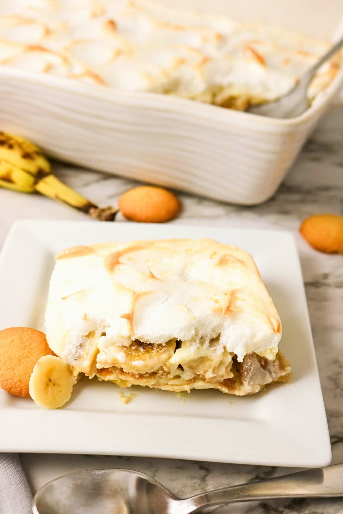Slice of banana pudding with wafers and banana on a white square plate.