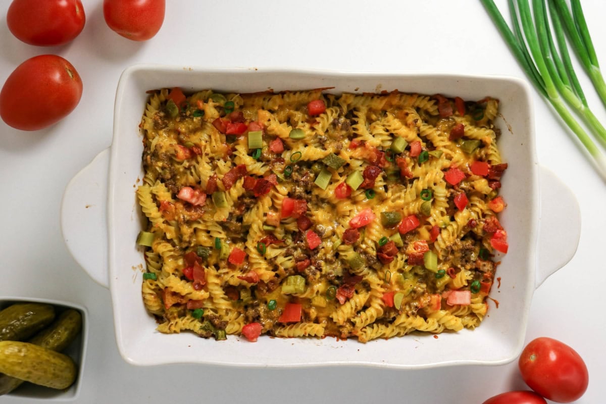Baked pasta casserole with diced tomatoes and green onions in a white dish.