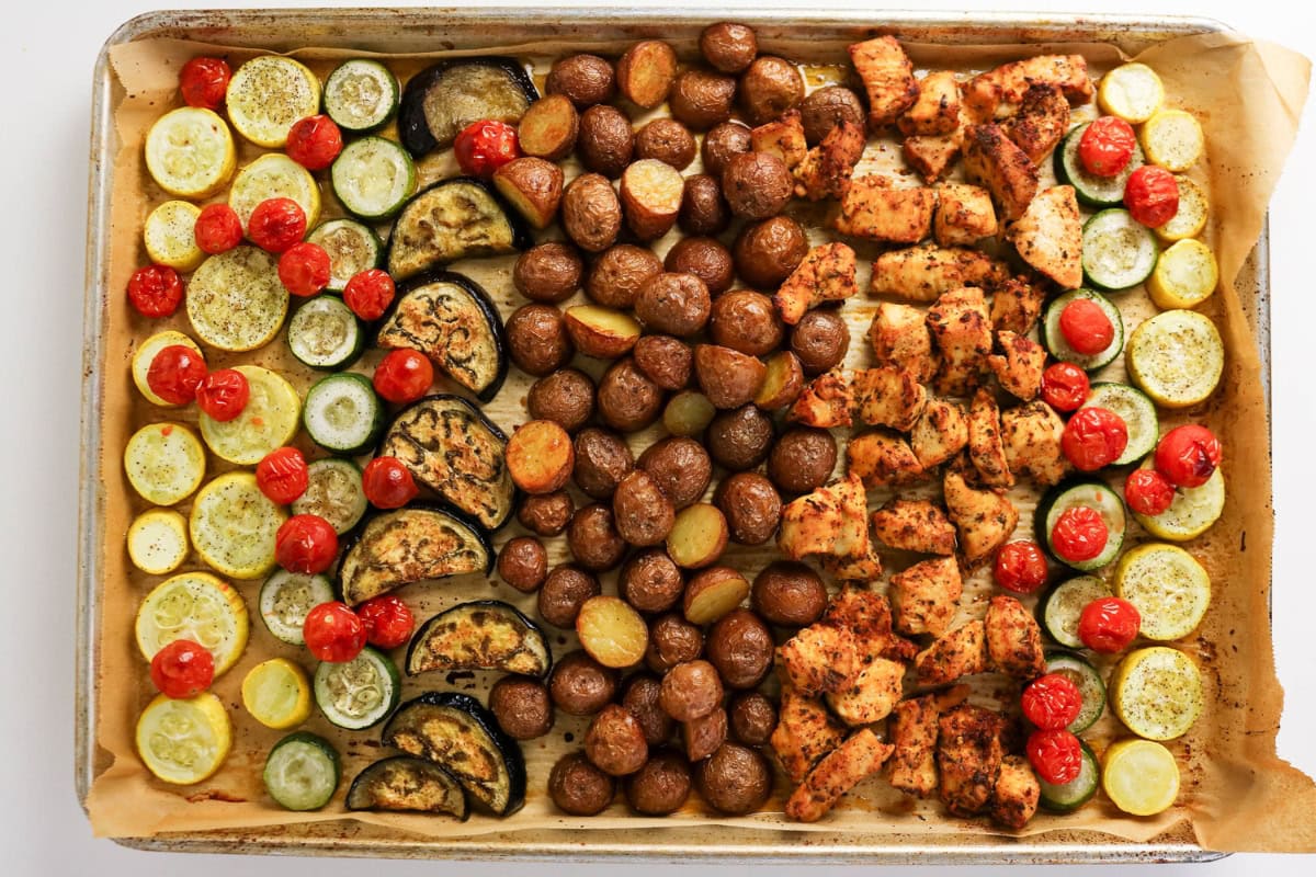 Sheet pan with roasted potatoes, squash, eggplant, tomatoes, and chicken pieces.