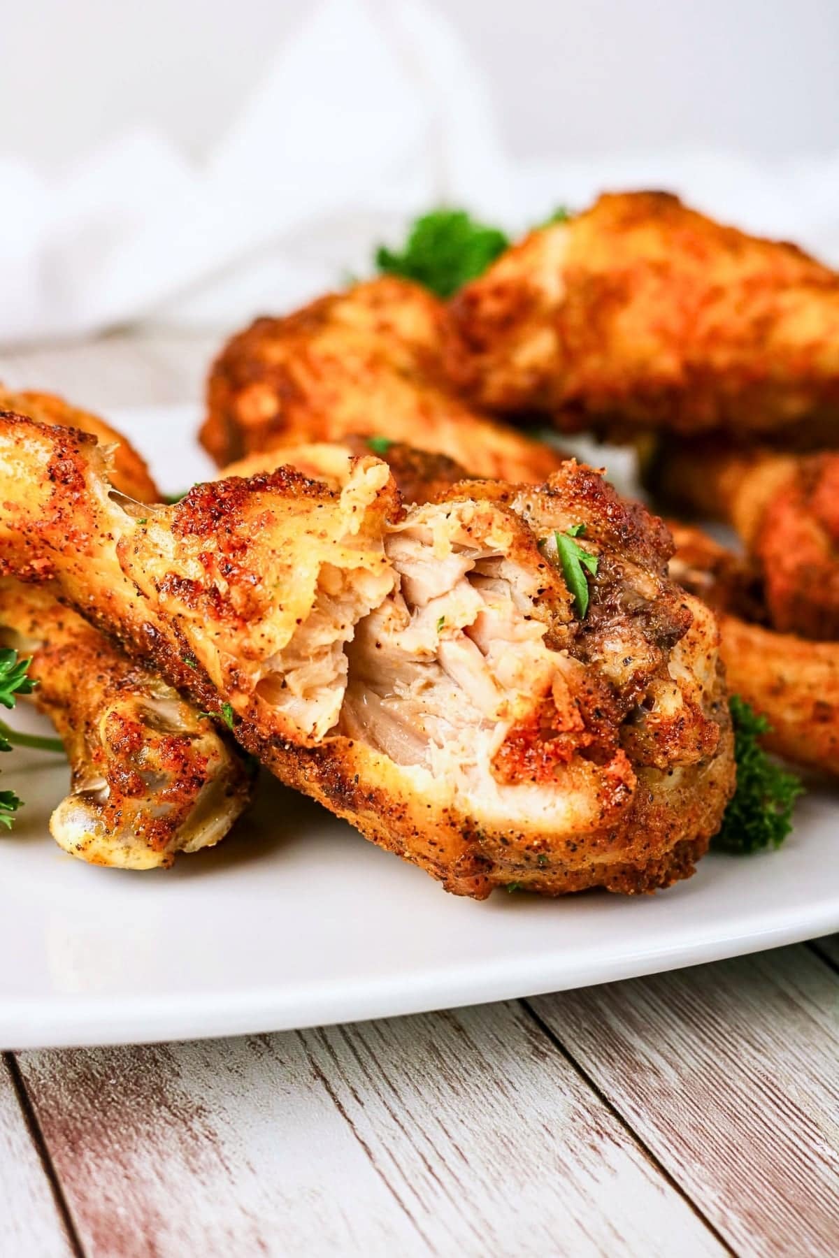 Seasoned baked chicken drumsticks on a white plate, one piece partially eaten.