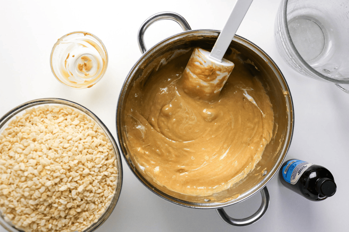 A pot of peanut butter mixture, rice cereal, vanilla, and a spatula on a table.