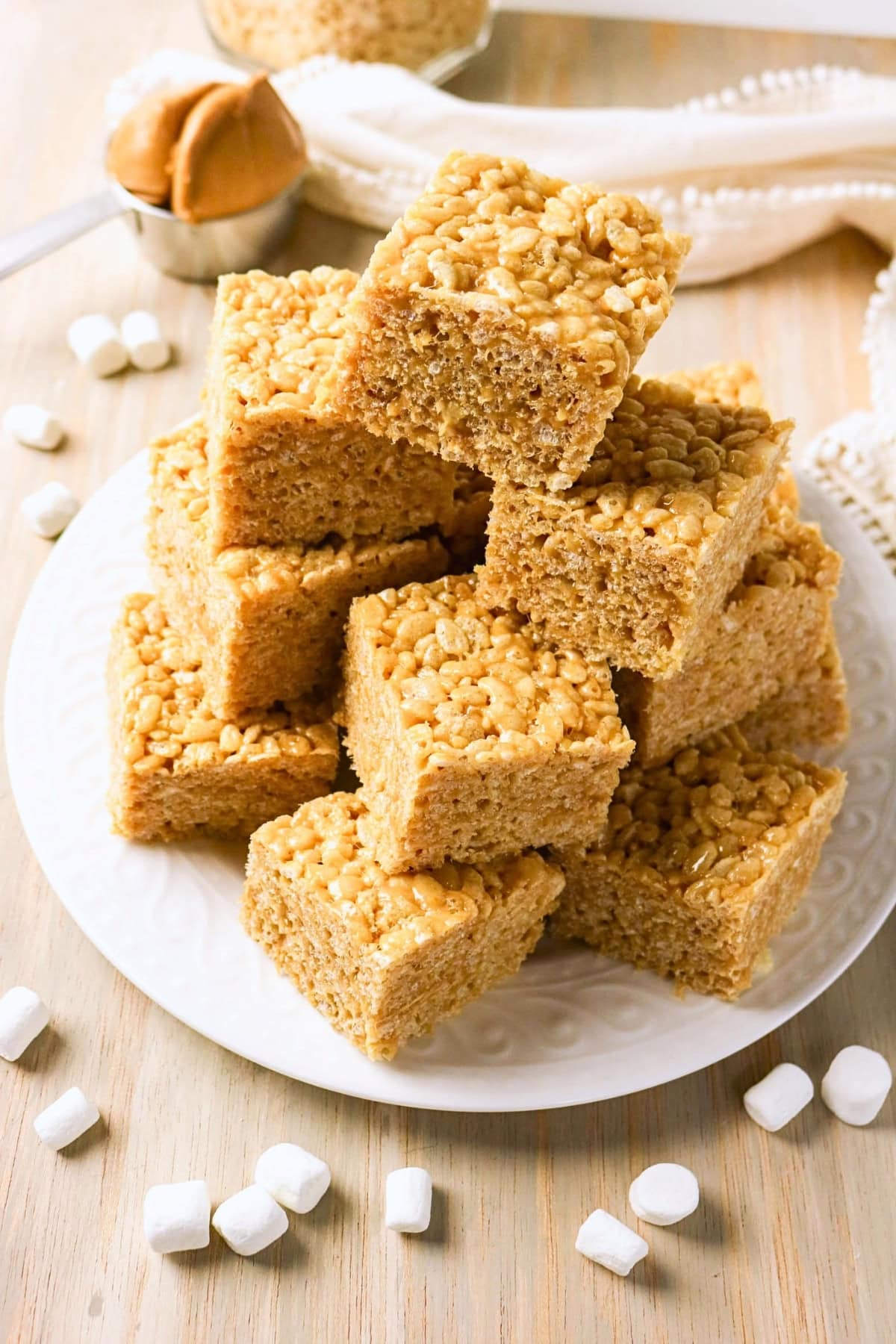 Stacked rice crispy treats on a white plate with marshmallows around.