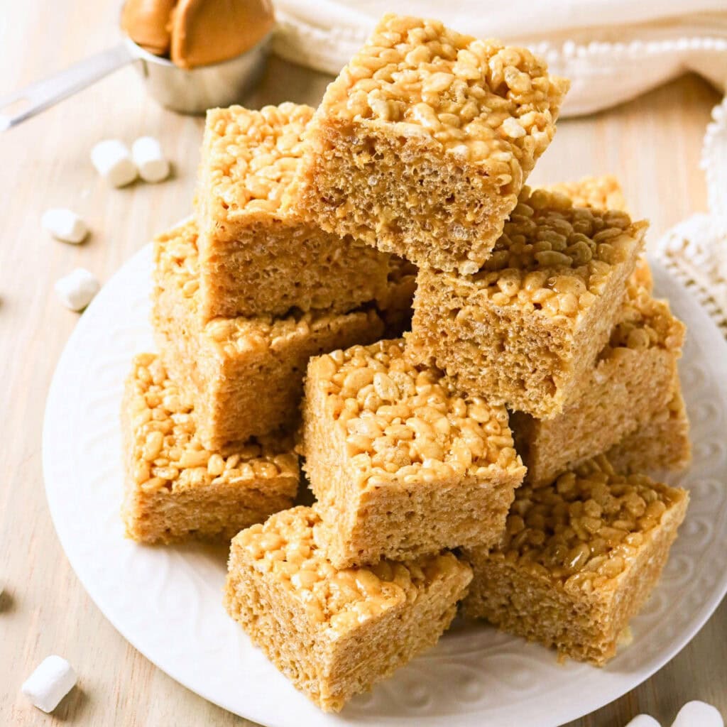 A plate stacked with rice crispy treats on a light wooden table.