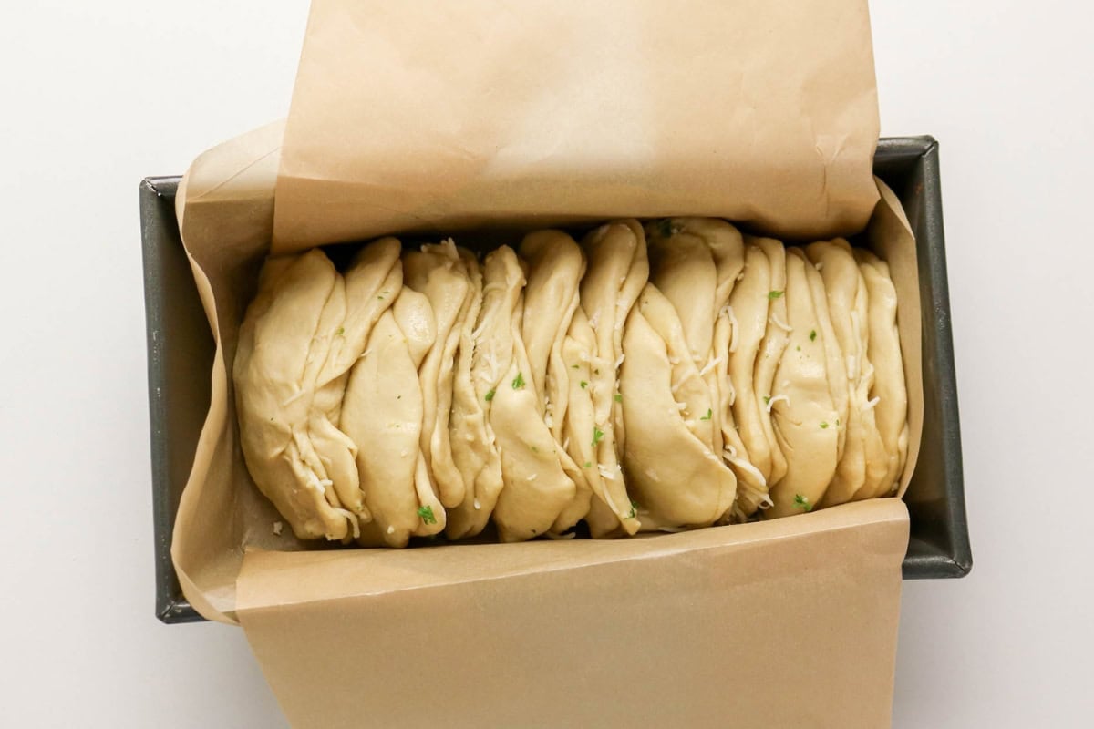 Unbaked pull-apart bread dough in a loaf pan lined with parchment paper.