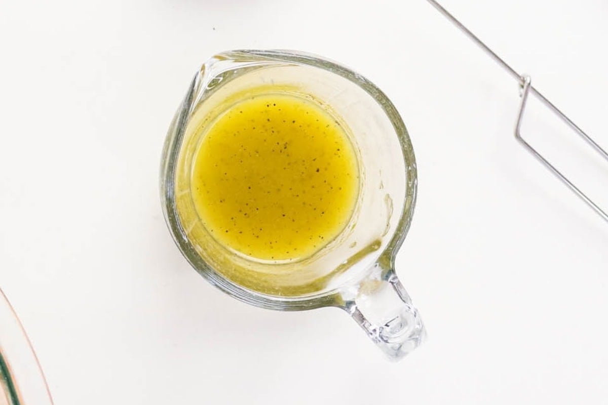 Glass measuring cup filled with yellow salad dressing on a white surface.