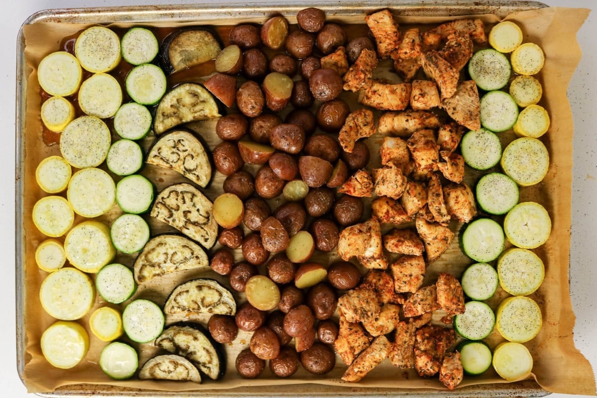 Sliced squash, eggplant, potatoes, and seasoned chicken on a sheet pan.
