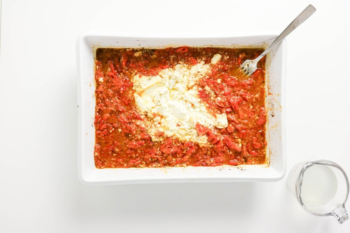 Baked tomatoes and feta cheese are ready to mix; milk is beside the dish.