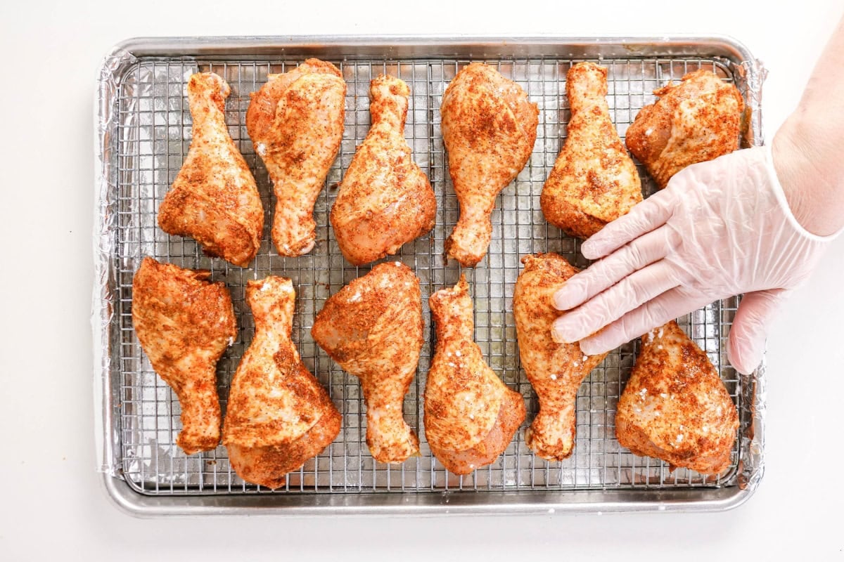 Gloved hand arranging seasoned chicken pieces on a wire rack for baking.