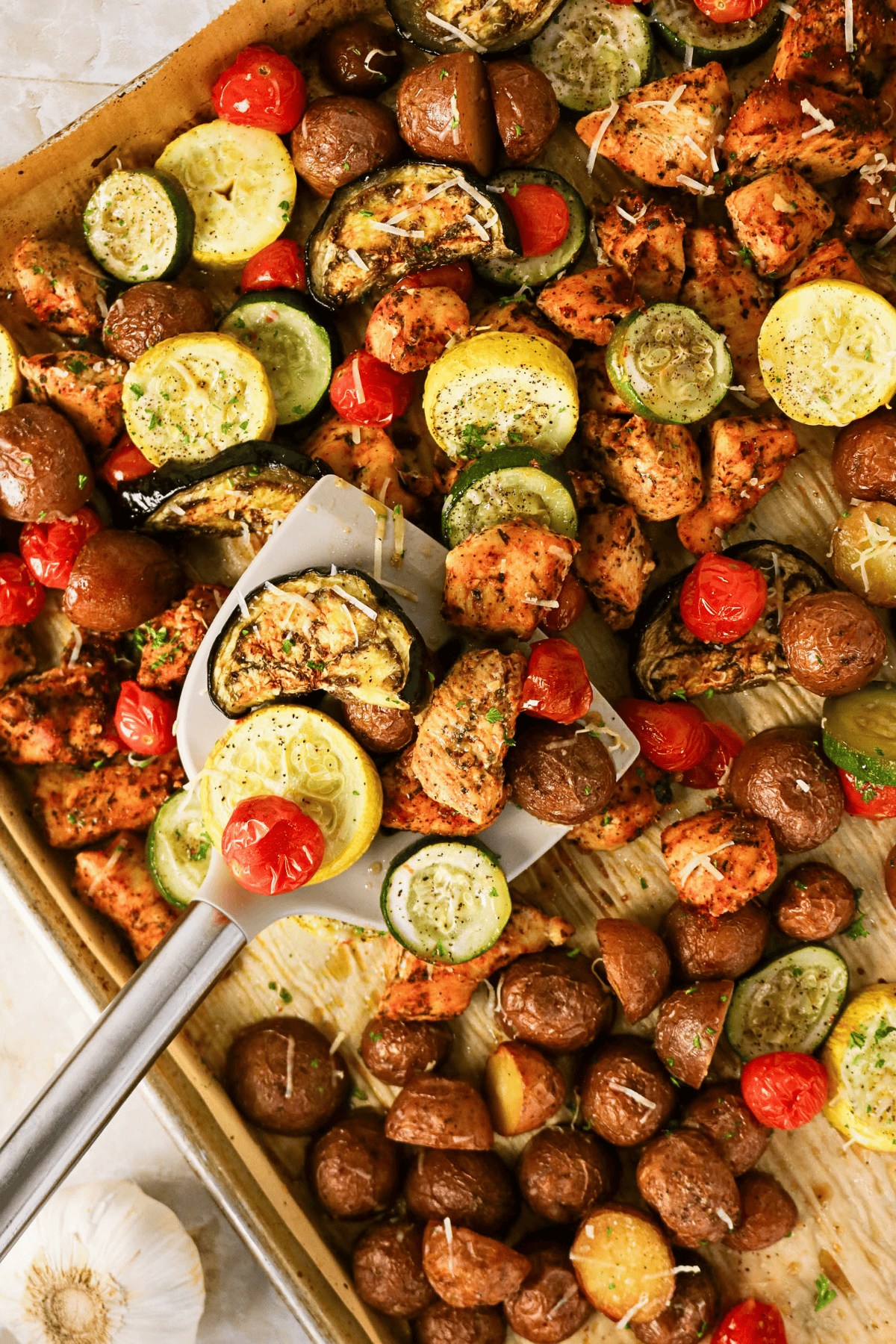 Sheet pan with roasted chicken, potatoes, squash, tomatoes, and zucchini.