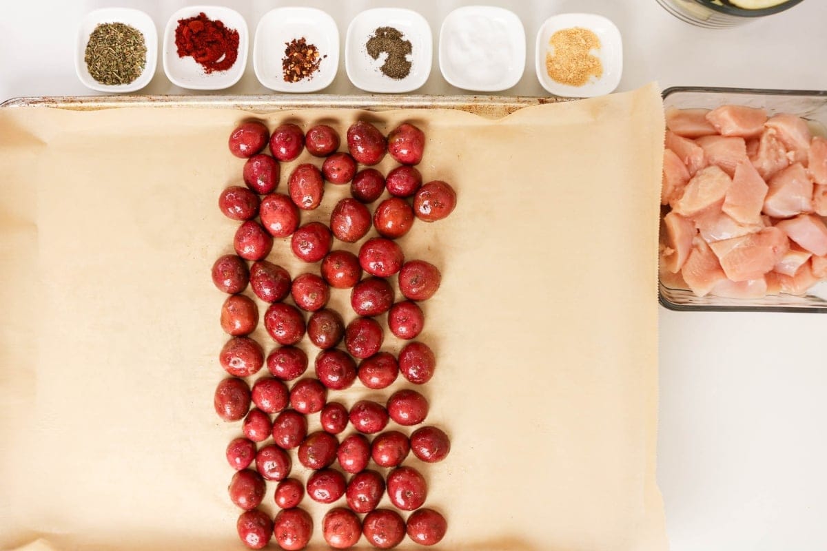 Red potatoes on parchment, spices in bowls, and cubed chicken in a glass dish.