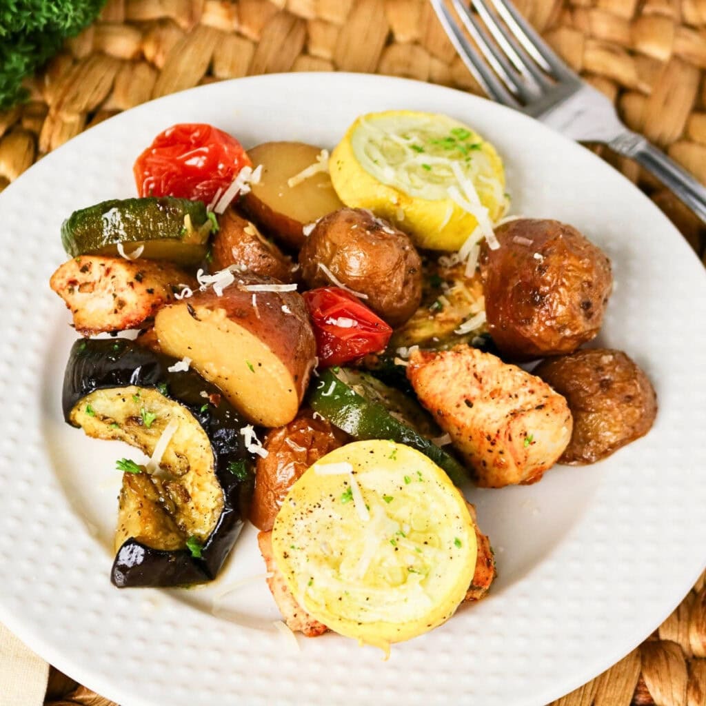 White plate with roasted potatoes, chicken, zucchini, yellow squash, and tomato.