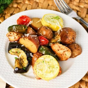 White plate with roasted potatoes, chicken, zucchini, yellow squash, and tomato.
