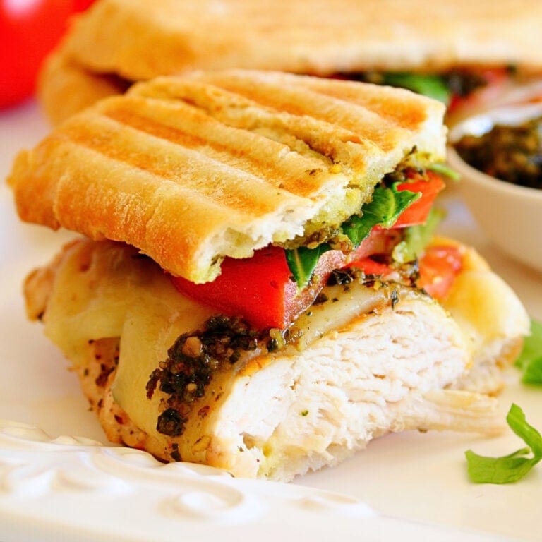 Grilled panini with turkey, cheese, tomato, greens, and pesto on a white plate.