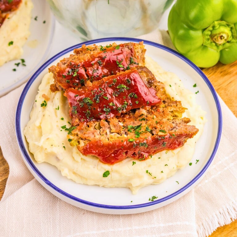 Slices of meatloaf with ketchup glaze on mashed potatoes, garnished with herbs.