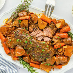 Pot roast with carrots, potatoes, herbs, and gravy on a white platter.