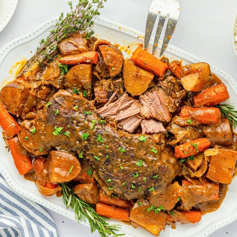 Pot roast with carrots, potatoes, herbs, and gravy on a white platter.