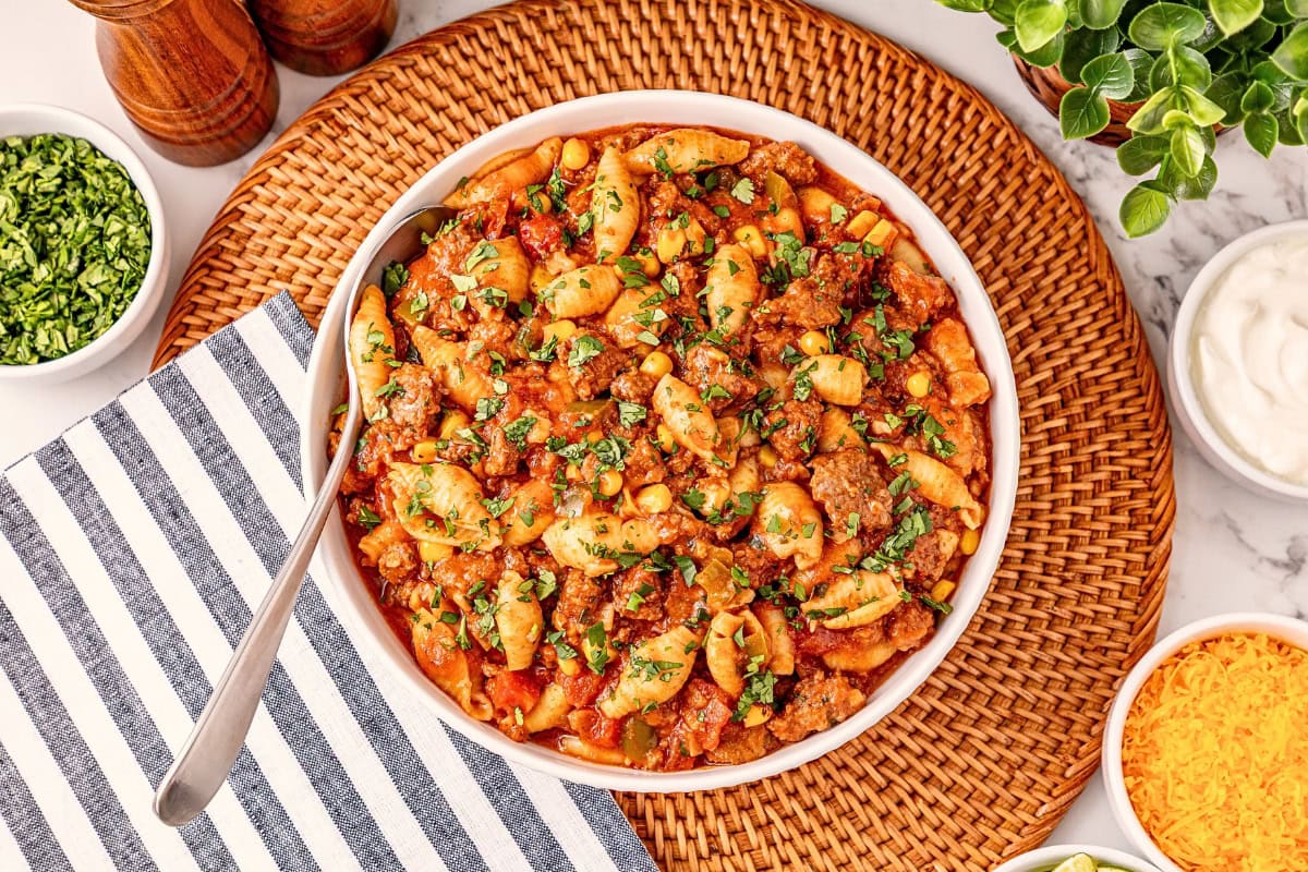 Bowl of pasta with ground beef, tomato sauce, and herbs on a woven placemat.