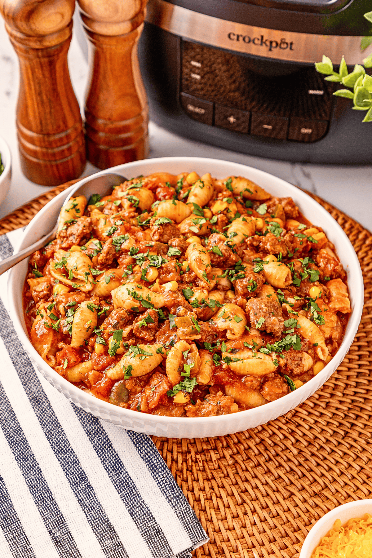 Pasta with meat sauce in a white bowl, topped with herbs, beside a crockpot.