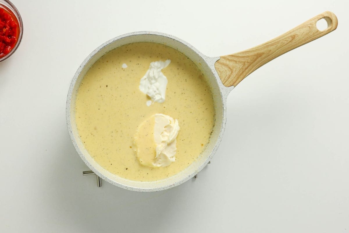 A white pan of creamy sauce with dollops of sour cream on a white background.
