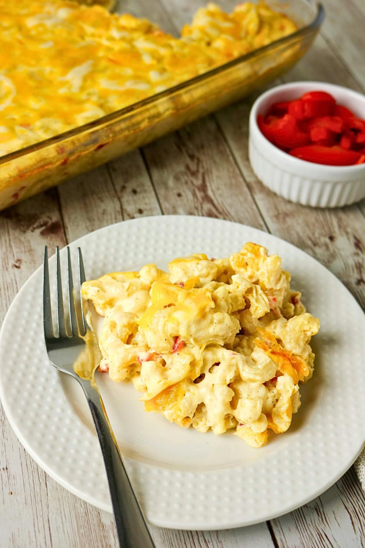 A plate of cheesy macaroni casserole beside sliced tomatoes in a ramekin.