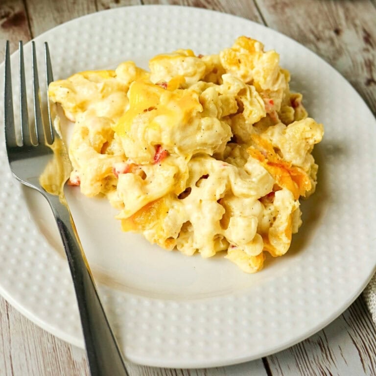 A serving of cheesy macaroni and cheese on a white plate with a fork.