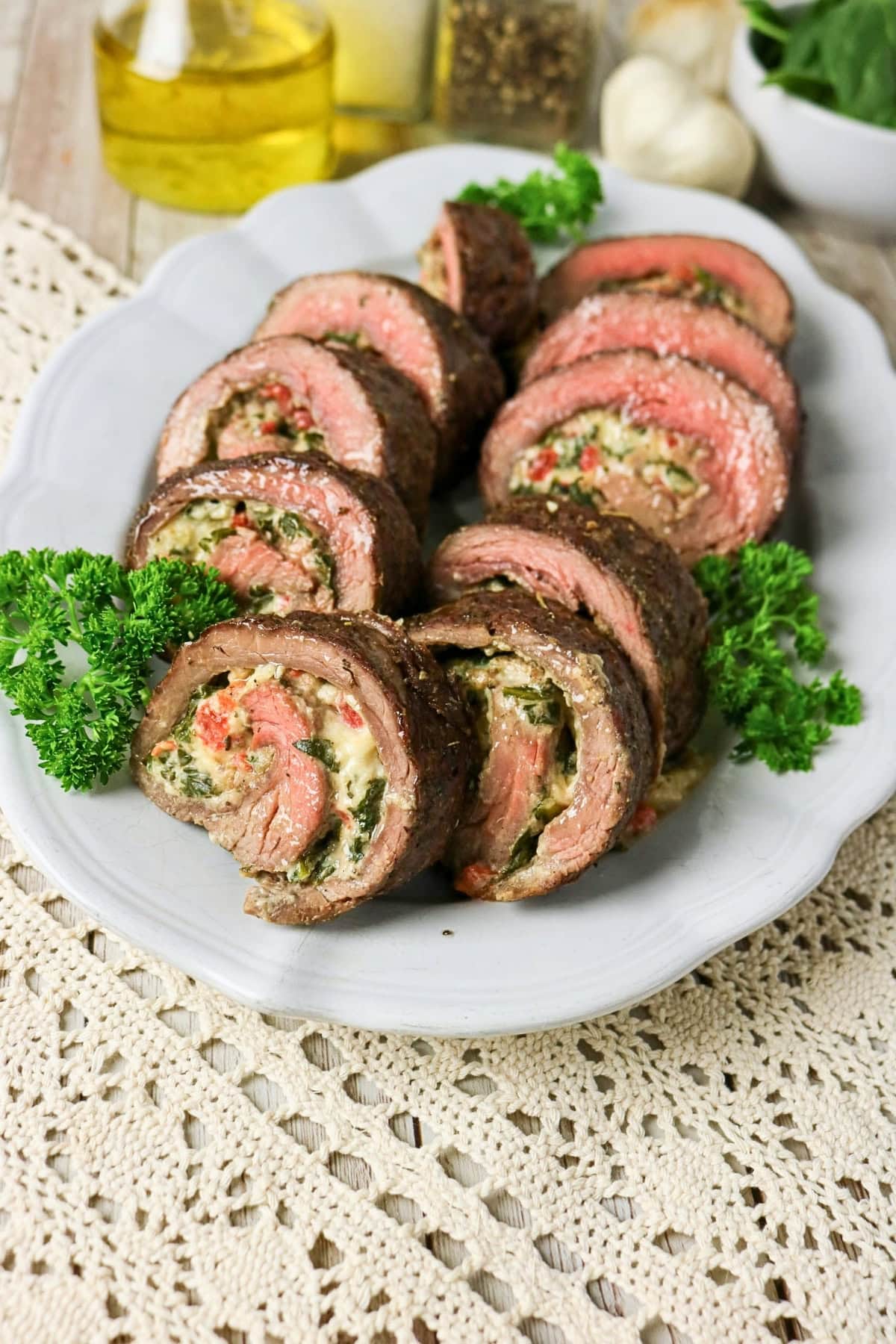 Sliced stuffed steak rolls on a white plate, garnished with parsley.