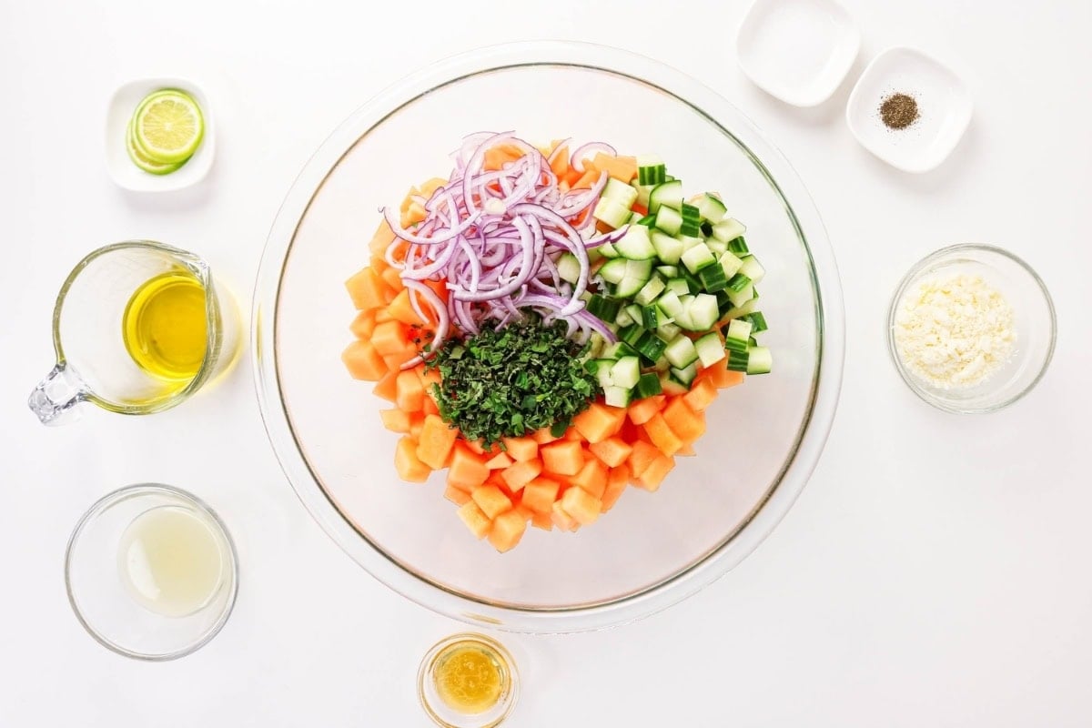 Chopped veggies, herbs, and dressings arranged in bowls on a white background.