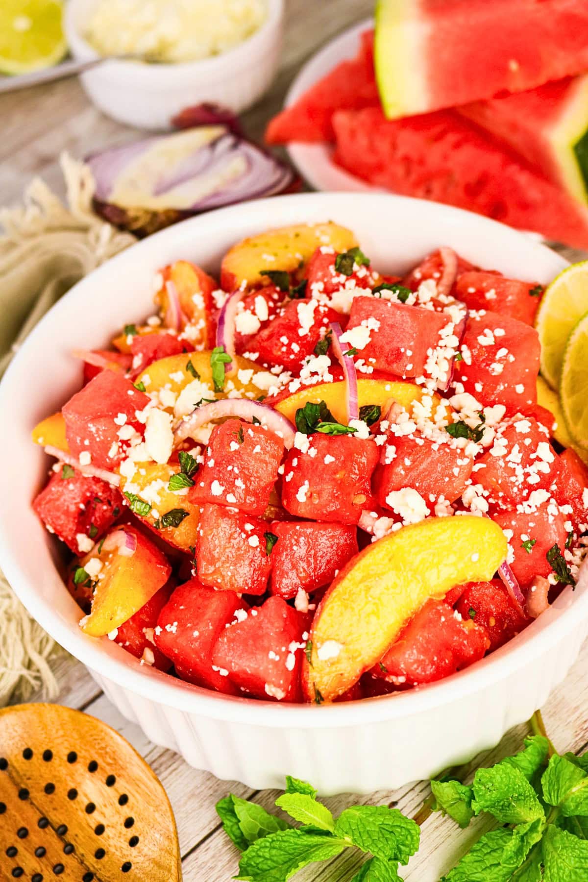 Watermelon and peach salad with feta, onions, herbs, and lime in a white bowl.