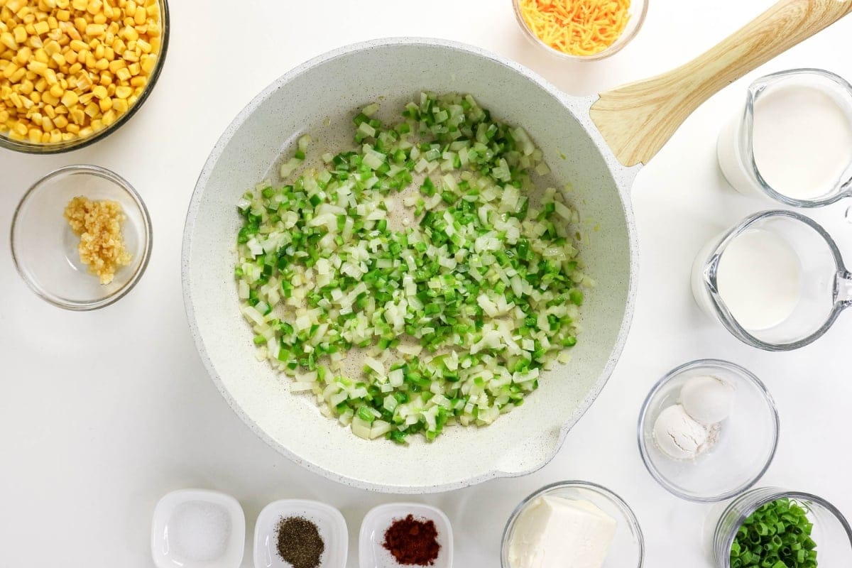 Chopped green veggies in a white skillet surrounded by ingredients in bowls.