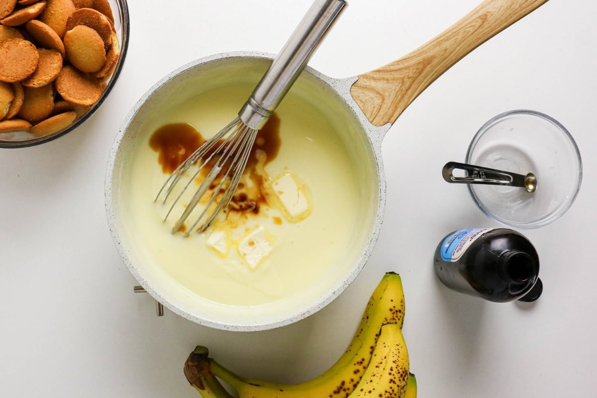 Whisk mixing pudding with butter and vanilla, surrounded by banana and cookies.
